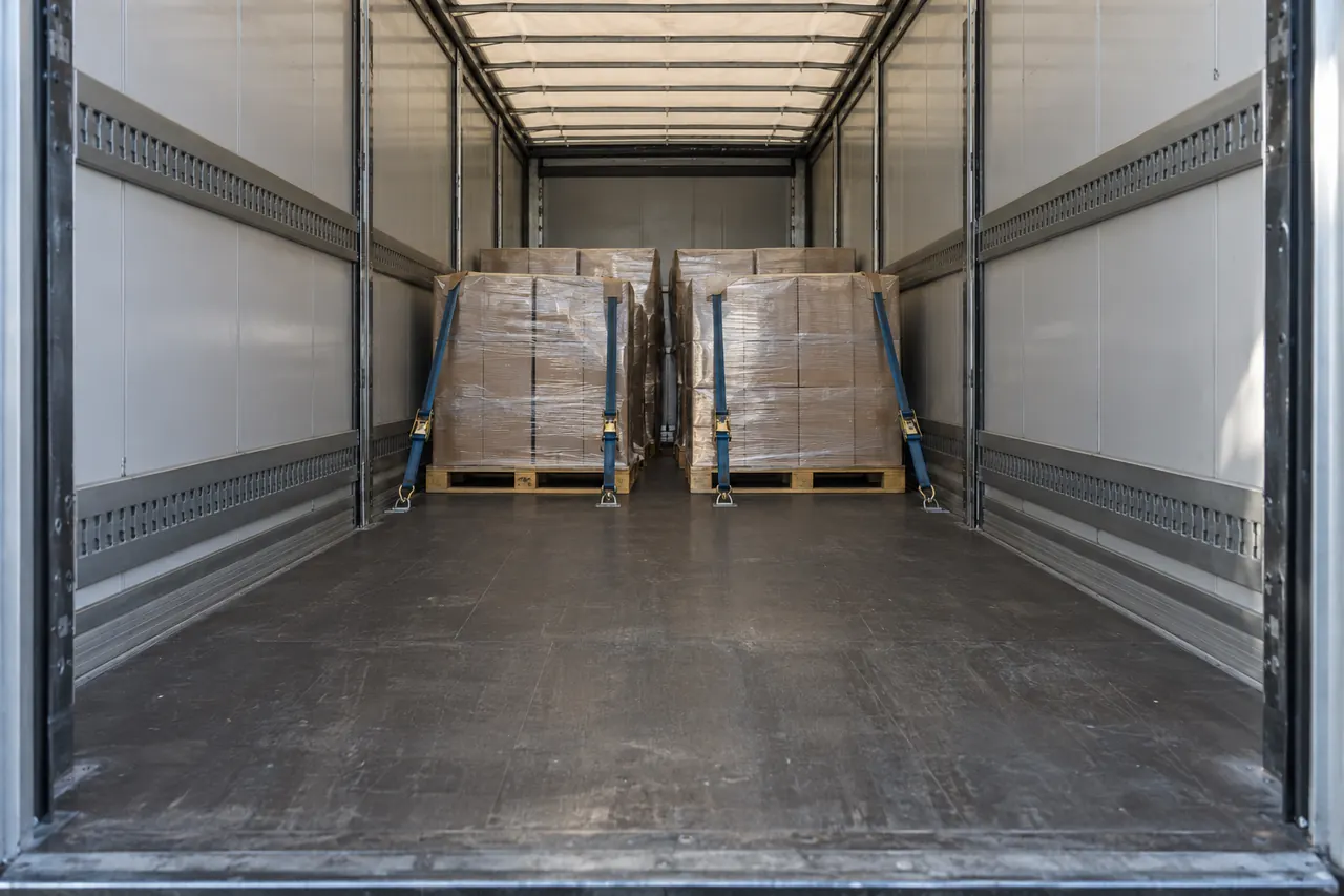 Tráiler a medio cargar con los palets bien trincados y luz natural entrando por las puertas traseras.